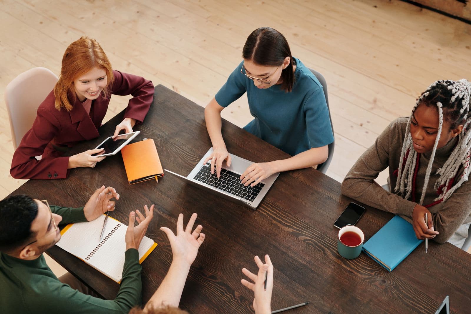 Colleagues discussing ideas with laptops and notebooks around a wooden table