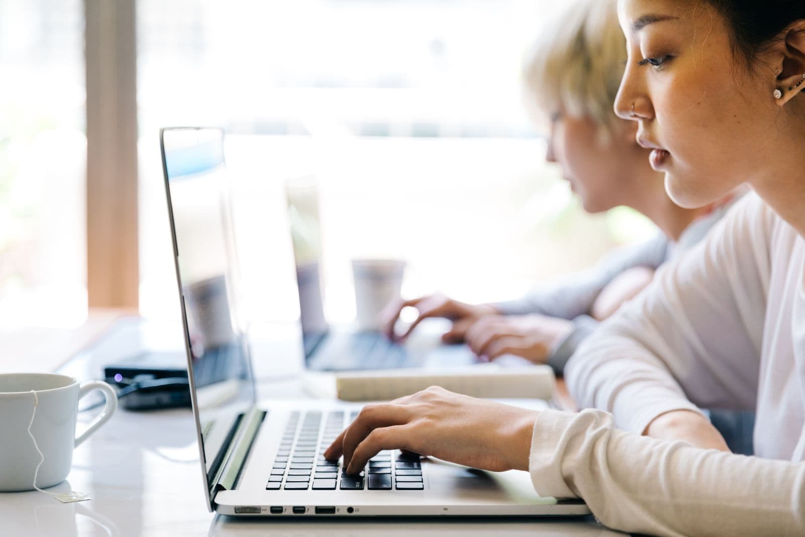 Two people concentrating on their laptops beside a window