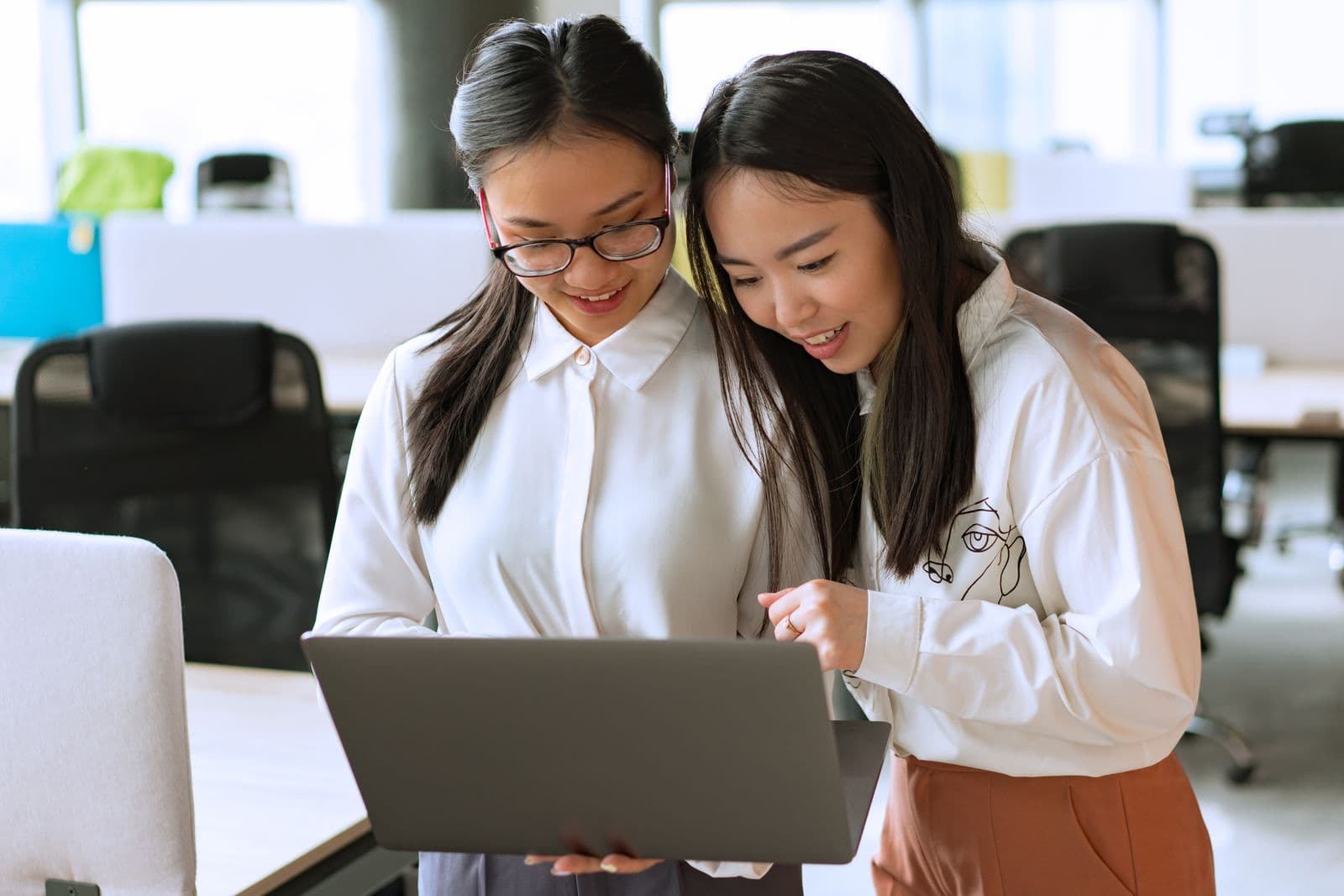Two colleagues reading a laptop screen together in their office