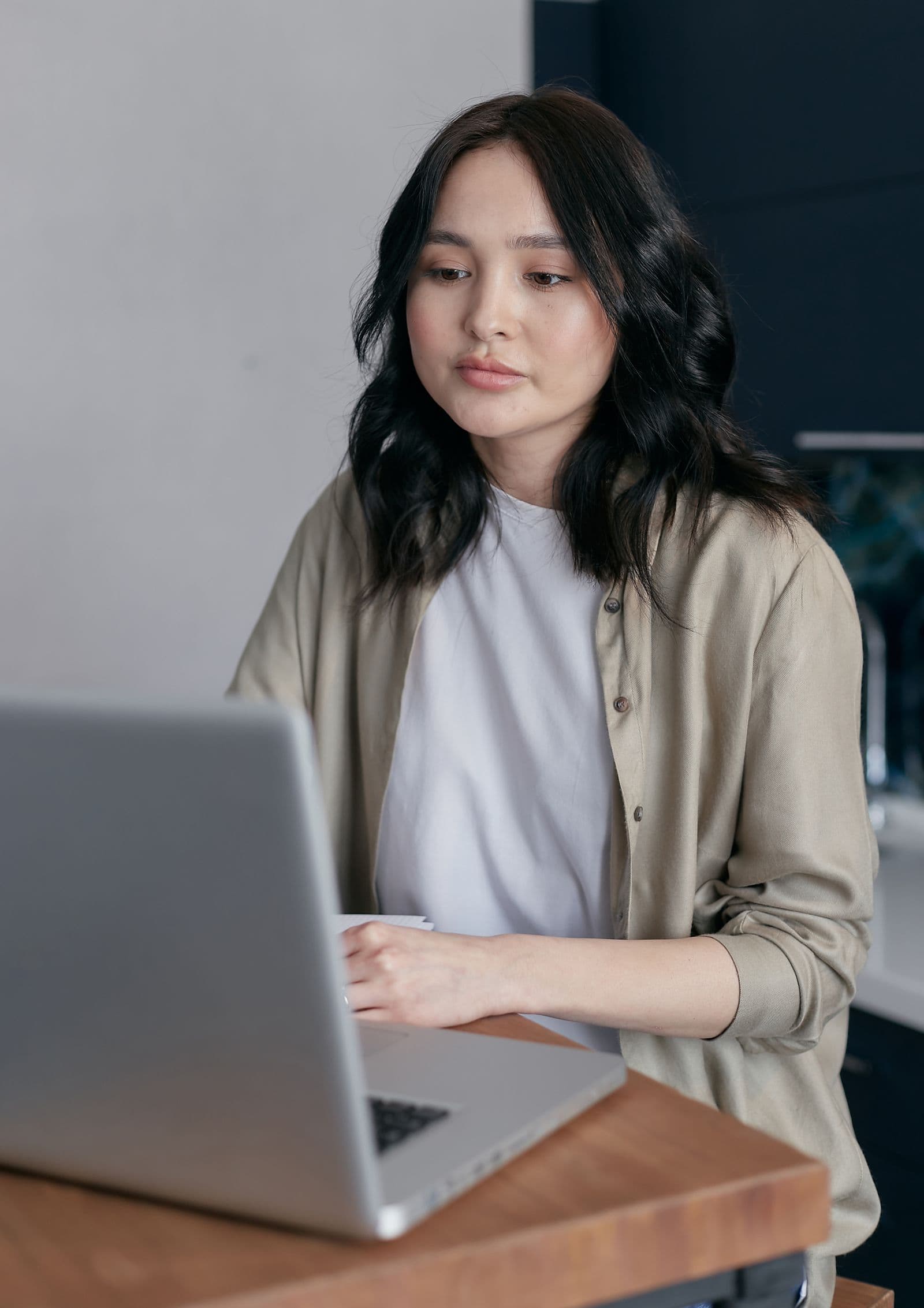 Woman in a beige cardigan working at a laptop on a wooden desk